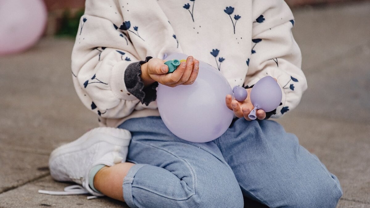 Criança com roupa infantil segurando balões na mão